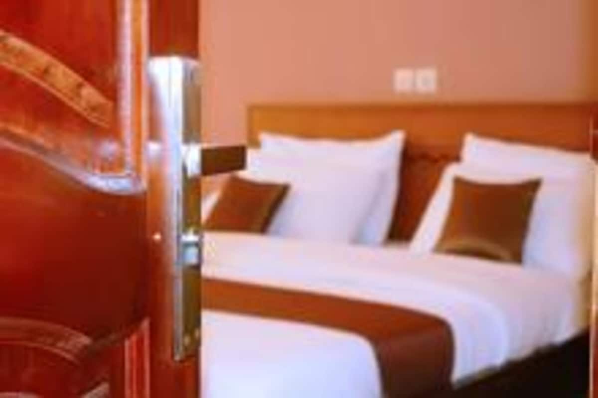 Une chambre d’hôtel avec une porte en bois, un lit avec une literie blanche et des oreillers marron, et une tête de lit en bois.
