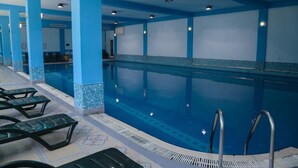 Una gran piscina coberta amb parets i terra de rajola blava. Hi ha diverses gandules i una escala de piscina.