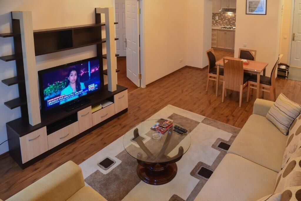 Una sala de estar con un televisor sobre un mueble bajo, una mesa de comedor con sillas y un sofá.