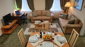 Habitació d'hotel amb taula de dinar preparada per a quatre persones, un sofà, un televisor i un escriptori amb una làmpada.