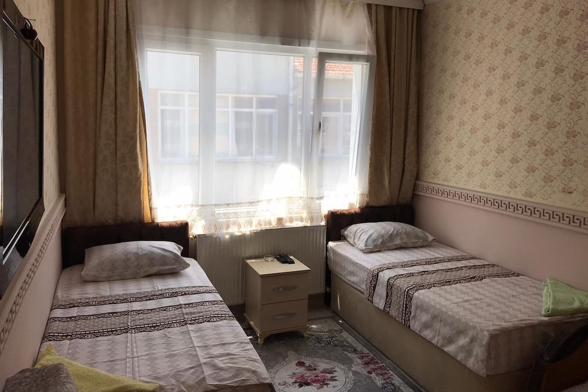 Une petite chambre confortable avec deux lits simples, une table de chevet et une fenêtre avec des rideaux.