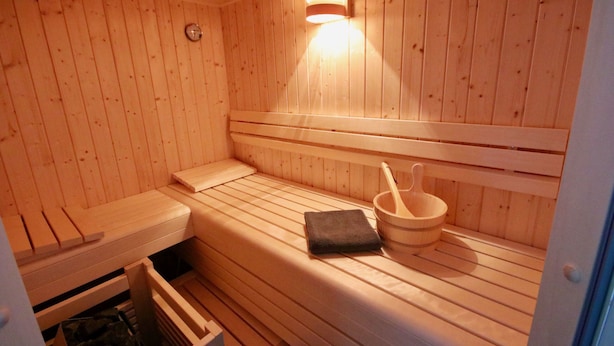 Una sauna in legno con panche, un asciugamano e un catino di legno.