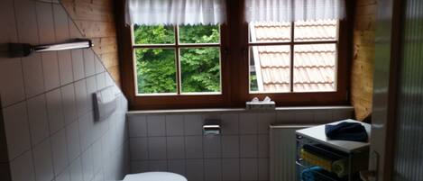 A small bathroom with a toilet, a window with a view of greenery, and a radiator.