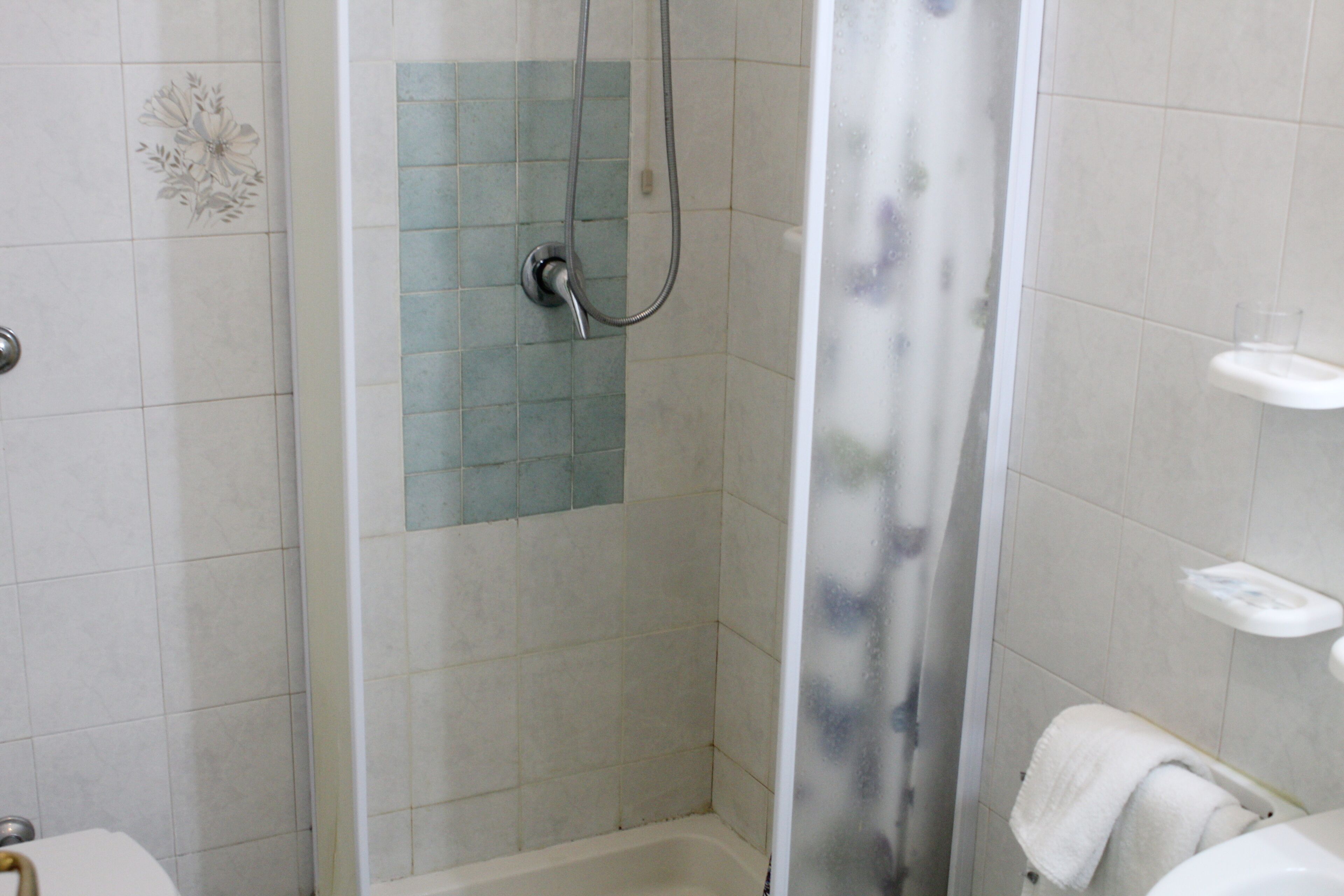 A shower with a glass door, a white bathtub, and a small white shelf with toiletries.