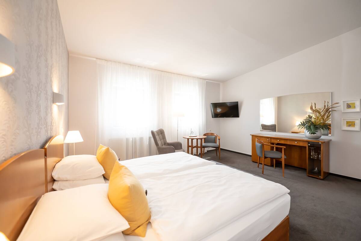 A hotel room with a bed, a desk, a chair, a TV, and a window with curtains.