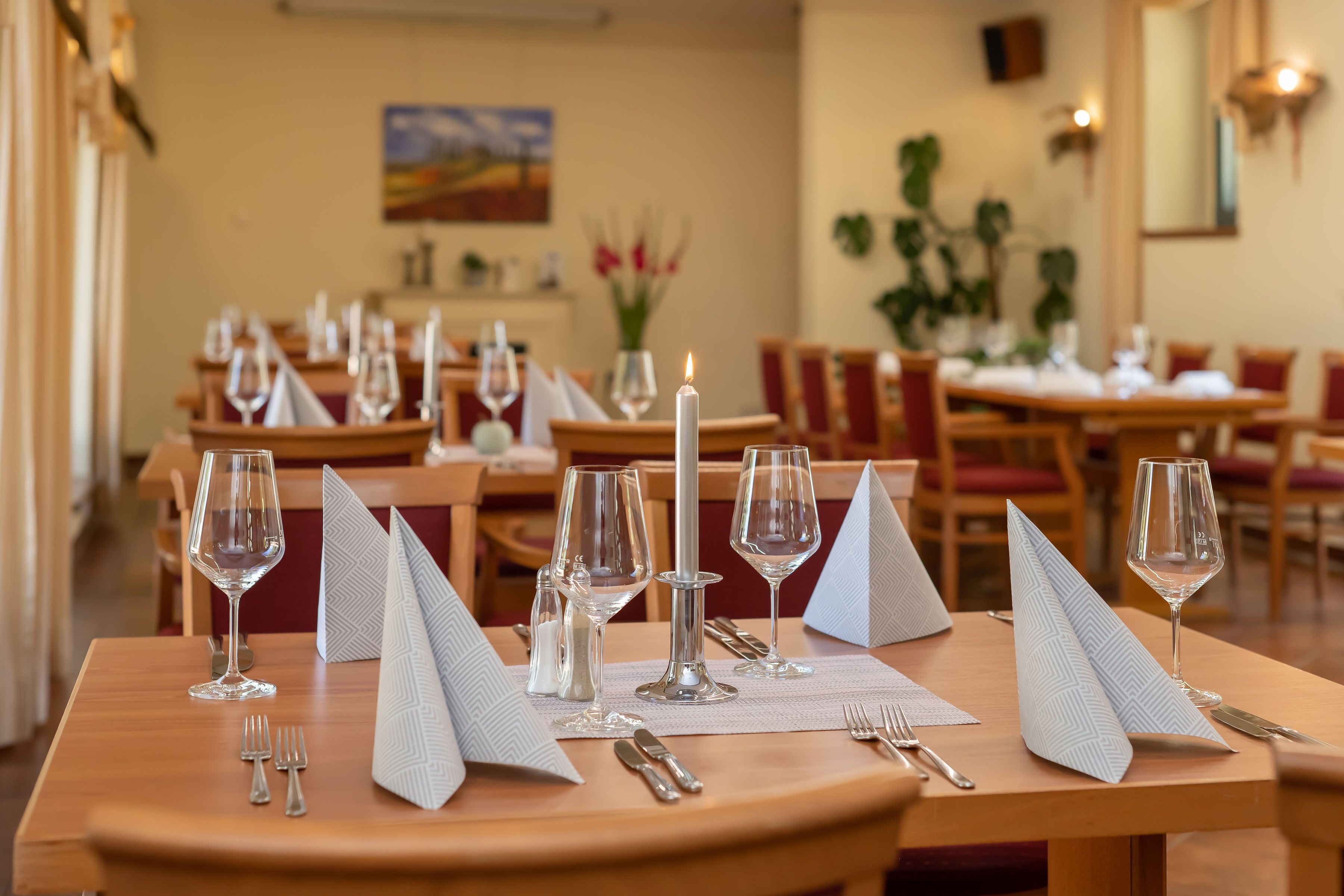 Een eetruimte met tafels voor twee personen, elk met wijnglazen, bestek en servetten.