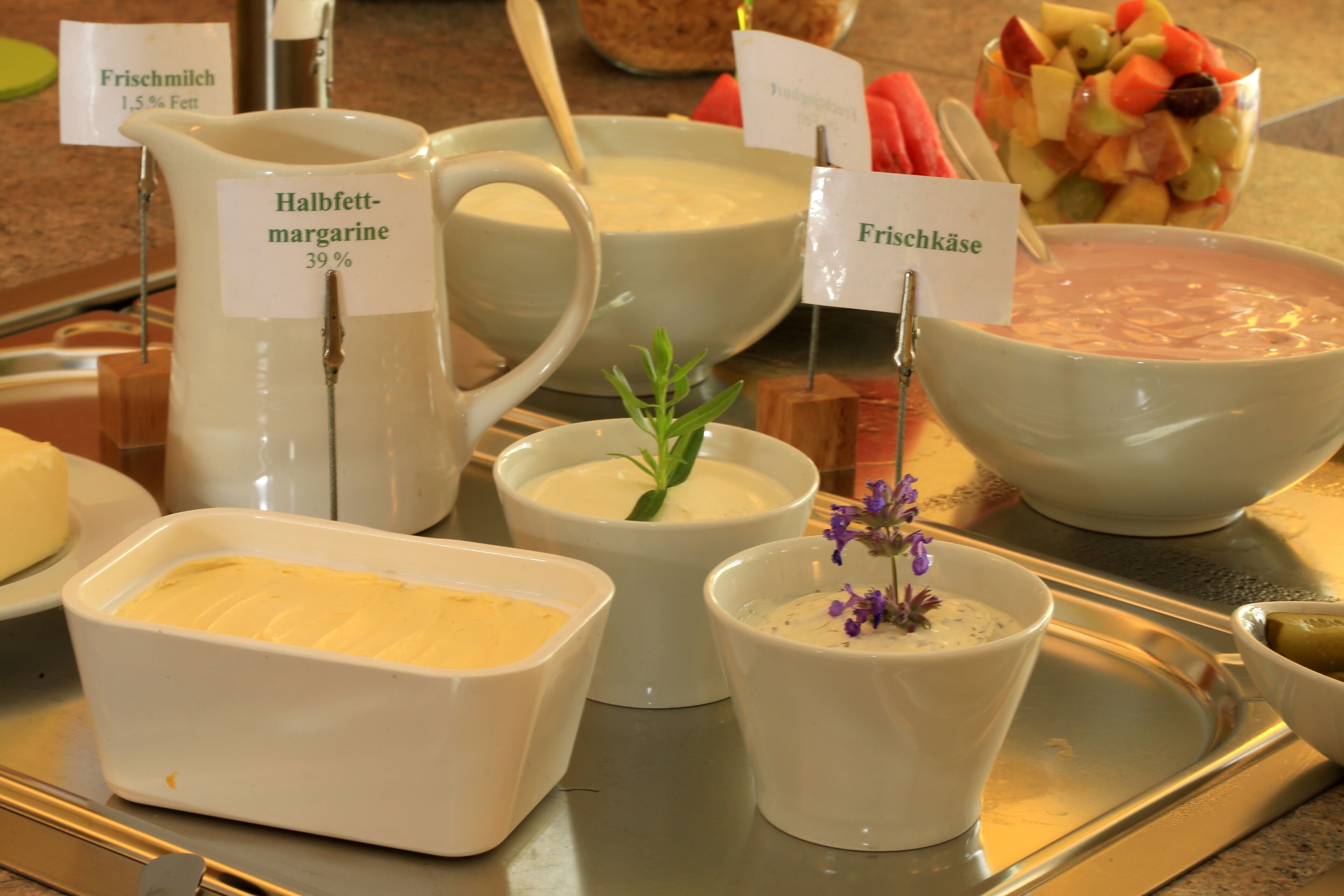 Verschiedene Speisen, darunter ein Krug Halbfettmargarine, eine Suppenschüssel und eine Obstsalatschüssel.