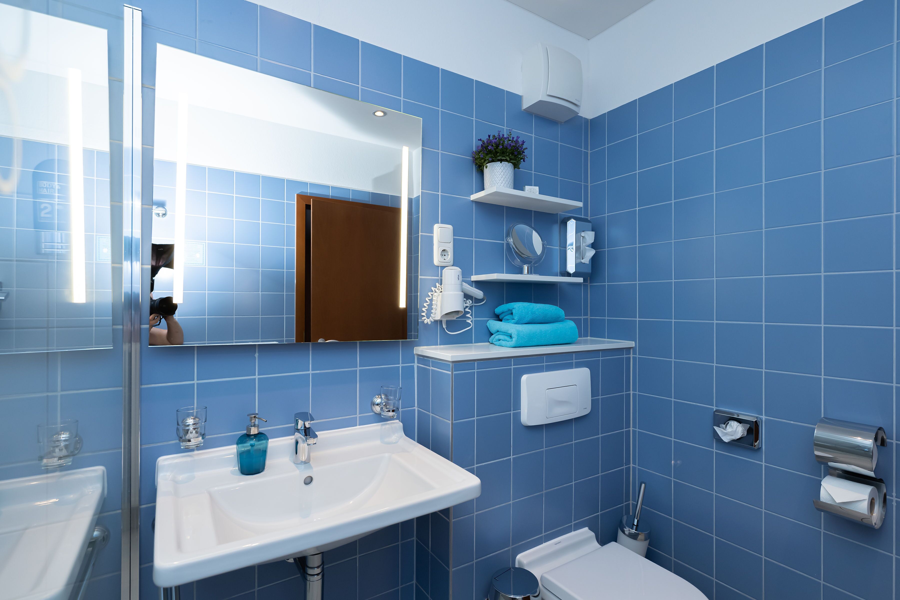 A bathroom with blue tiles, a white sink, a mirror, a towel rack, and a toilet.
