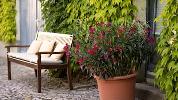 A bench with cushions, a potted plant with pink flowers, and a cobblestone path.