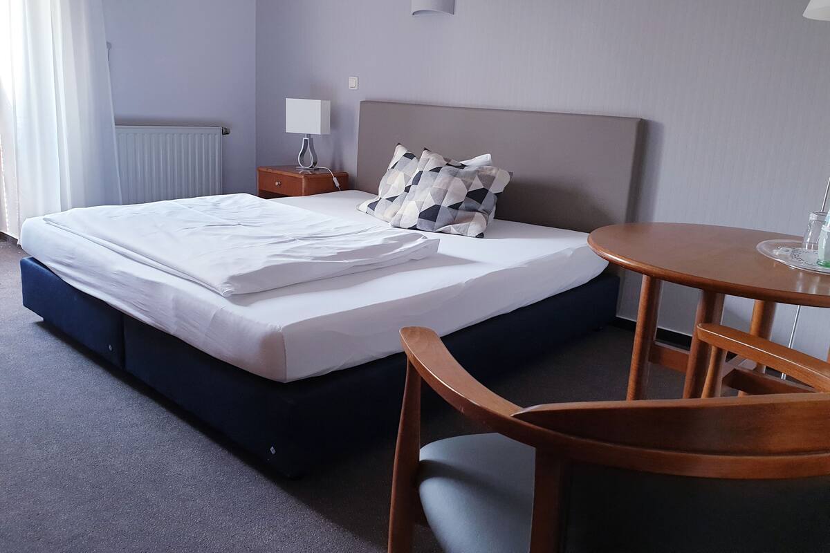A hotel room with a bed, bedside table, lamp, and a small round table with chairs.