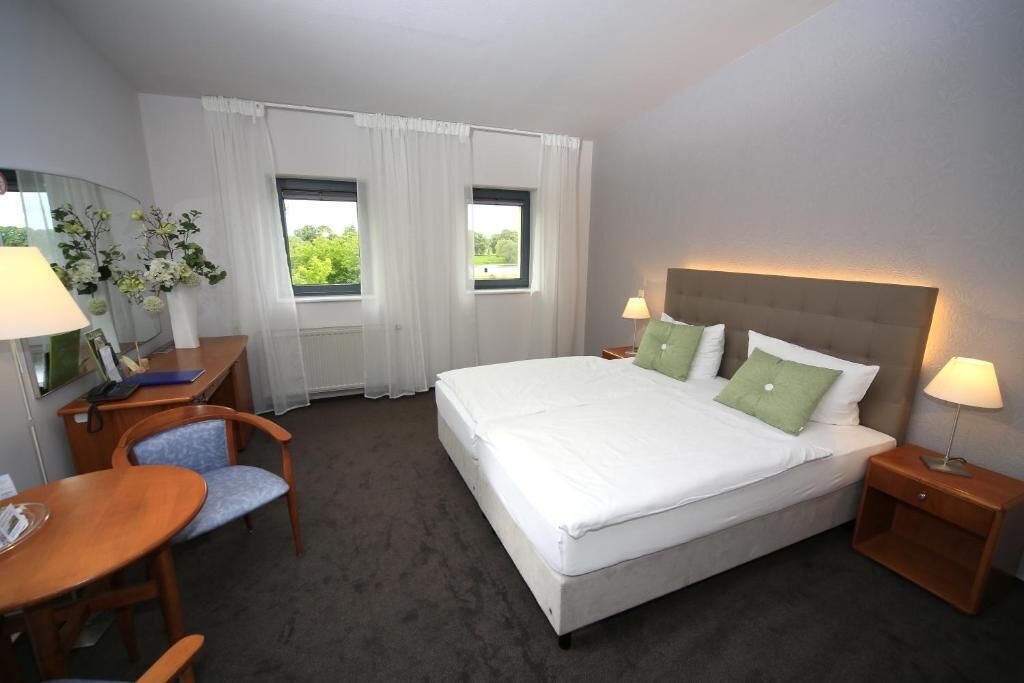 Ein Hotelzimmer mit Bett, Nachttischen, Schreibtisch, Stuhl und zwei mit Vorhängen versehenen Fenstern.