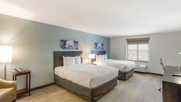 A hotel room with two beds, a desk, a chair, and artwork on the walls.