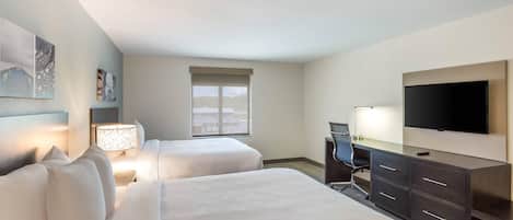 A hotel room with two beds, a desk, a chair, a TV, and artwork on the walls.