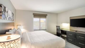 A hotel room with a bed, desk, chair, TV, and artwork on the wall.