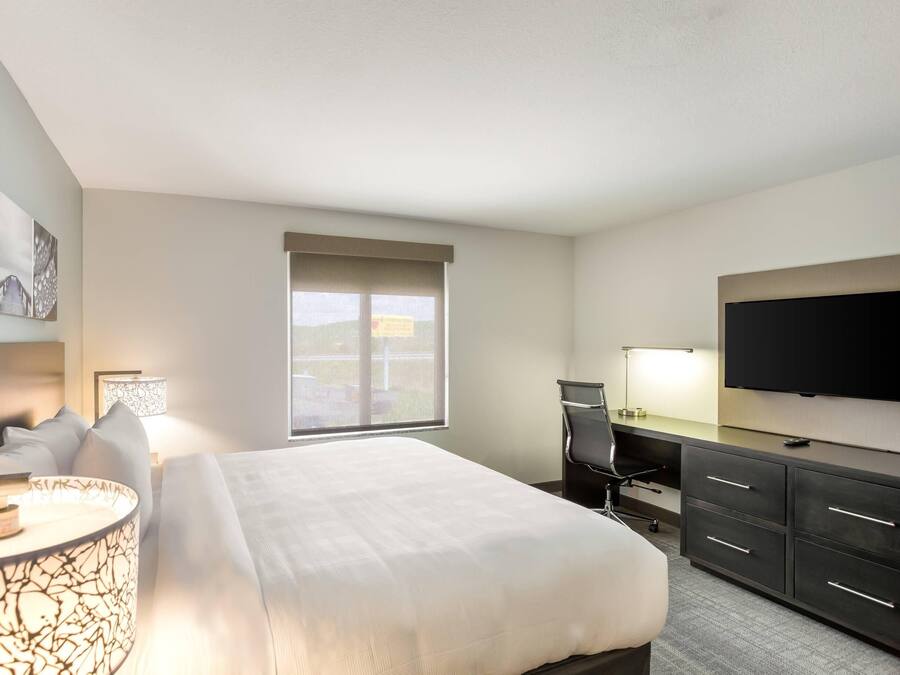 A hotel room with a bed, desk, chair, TV, and artwork on the wall.