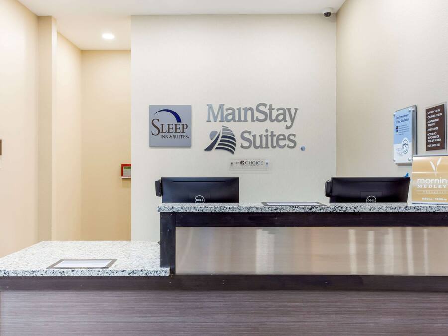 Um balcão de recepção de hotel com a placa da MainStay Suites e da Sleep Inn & Suites.