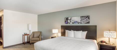A hotel room with a large bed, two bedside tables with lamps, a chair, and a wall art piece above the bed.