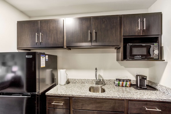 A kitchen with dark wood cabinets, a black refrigerator, a microwave, a sink, and a coffee maker.