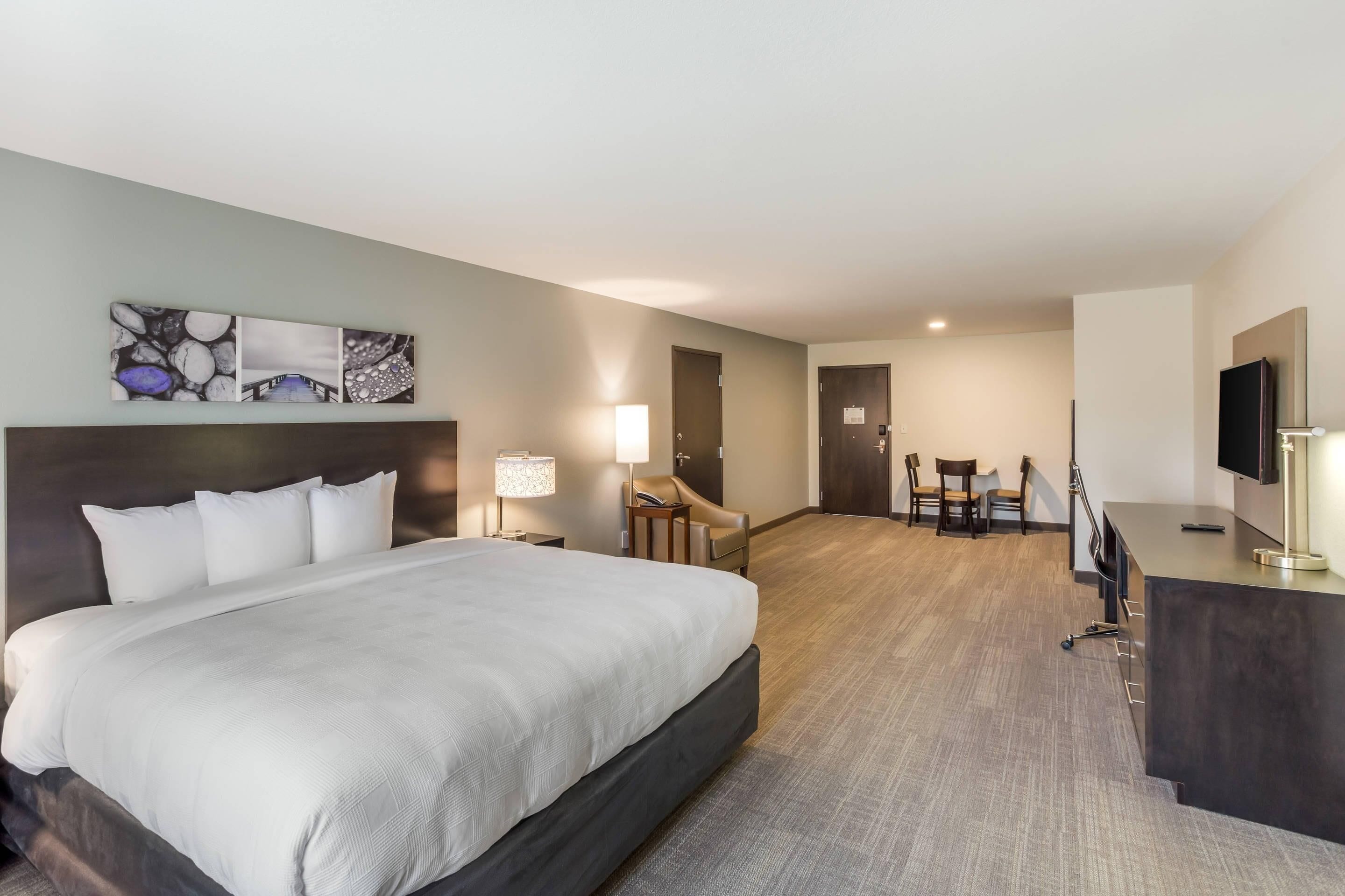 Een hotelkamer met een groot bed, een bureau, een stoel, een televisie en een schilderij aan de muur.