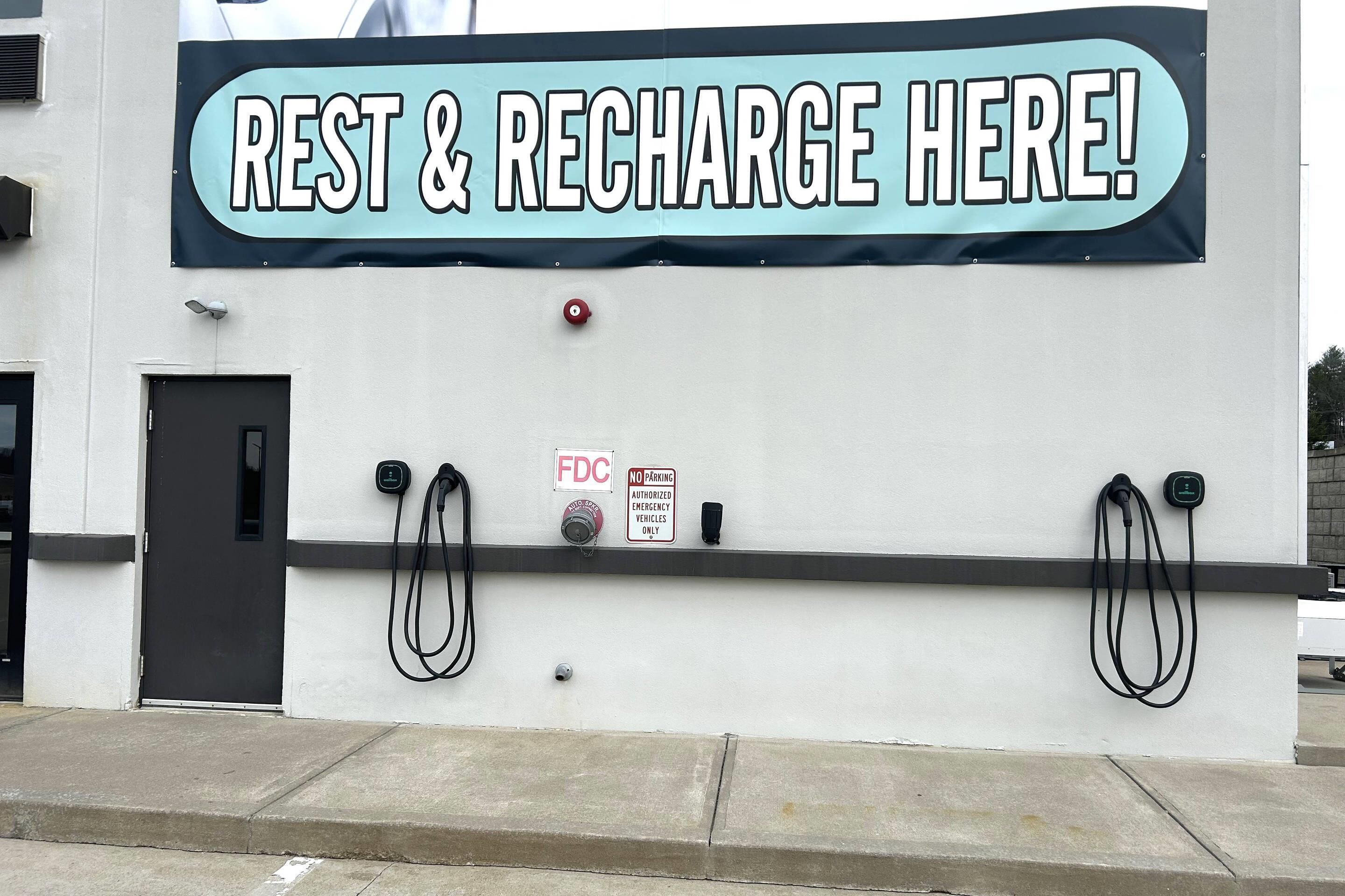 Un mur avec une pancarte indiquant « REPOSEZ-VOUS ET RECHARGEZ VOS BATTERIES ICI ! » et des bornes de recharge pour véhicules électriques.