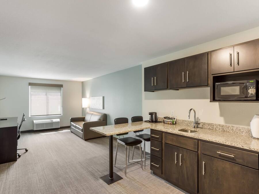 A modern kitchen with dark wood cabinets, a granite countertop, a microwave, and a coffee maker. There is a dining area with a table and chairs.