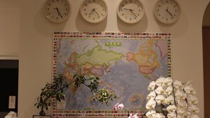Four clocks with city names above them, a world map, and two potted plants. - Guest House COCO Hiroshima - Hostel, Caters to Women (Hiroshima)