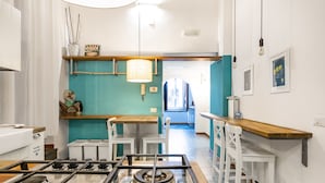 A kitchen with a gas stove, white chairs, a wooden table, and a teal accent wall. - Napoli Napoli (Naples)