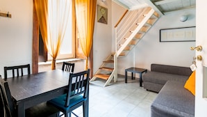 A dining area with a wooden table and chairs, a staircase, and a gray sofa. - Napoli Napoli (Naples)