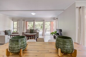 A modern living room with a wooden dining table, two green ceramic planters, a sofa set, and a television. - UniqueStay Mayfair Deluxe Apartment (Cape Town)