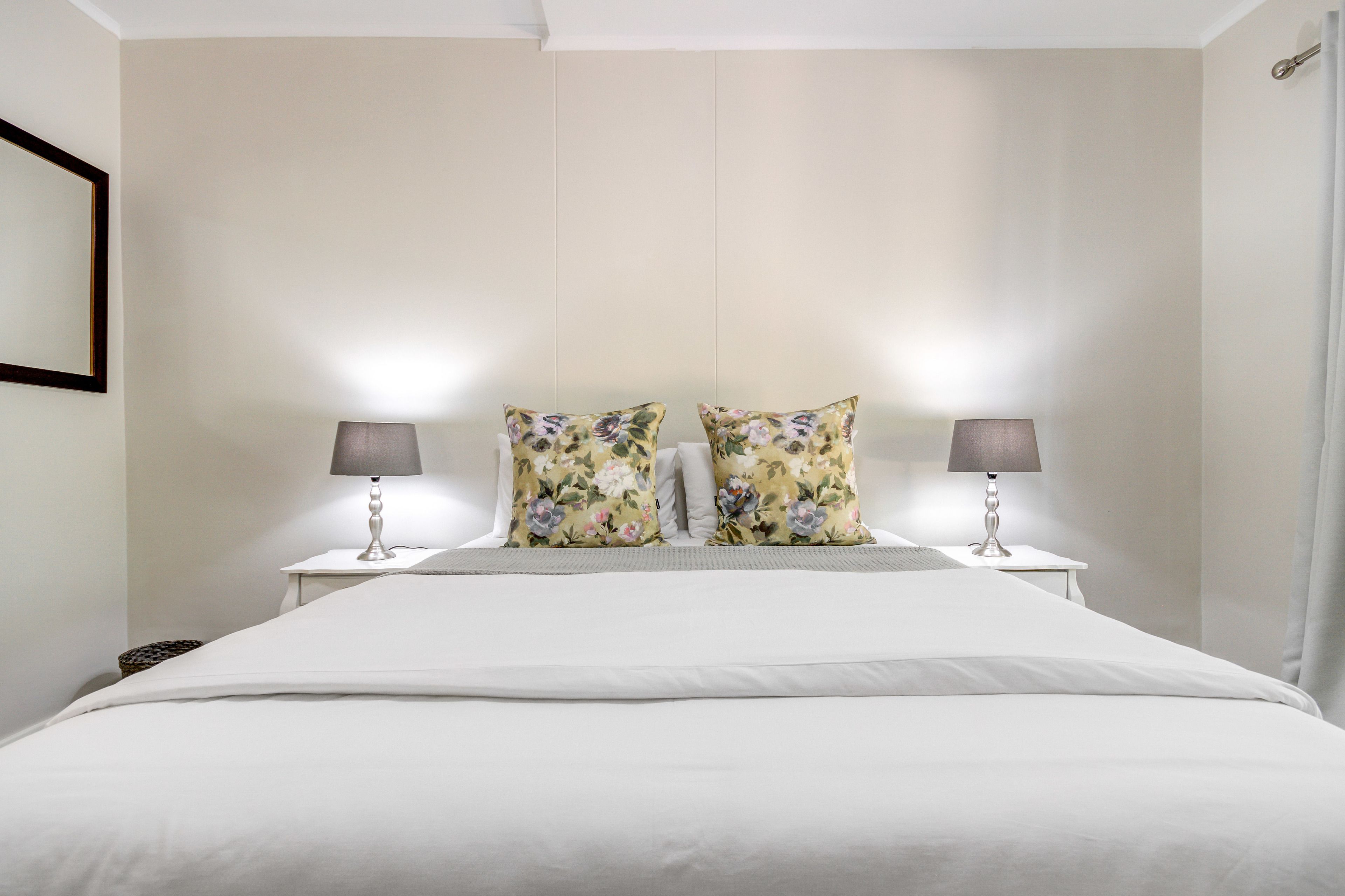 A neatly made bed with white linens and two floral pillows, flanked by two bedside lamps on white nightstands.