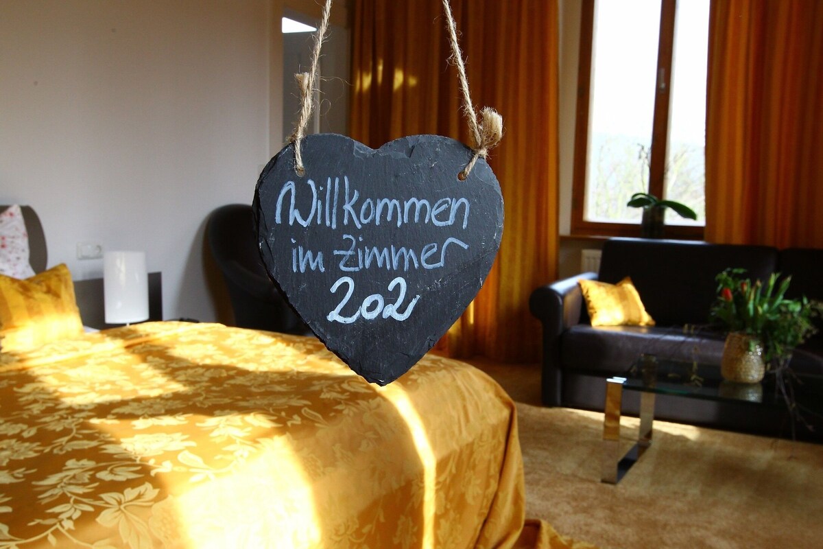 A room with a bed, a sofa, and a hanging sign with text.