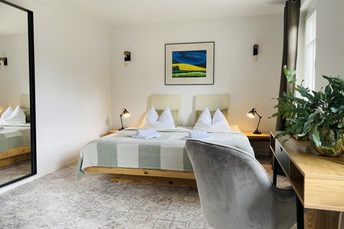 A neatly arranged bedroom with a bed, bedside tables, a desk, and a chair.