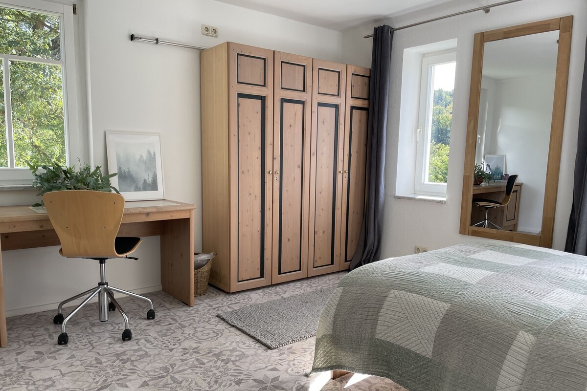 A bedroom with a bed, a desk with a chair, a wardrobe, and a large mirror.