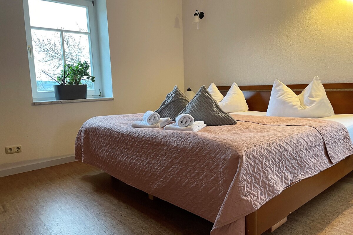 A neatly made bed with a pink quilt, pillows, and rolled towels.
