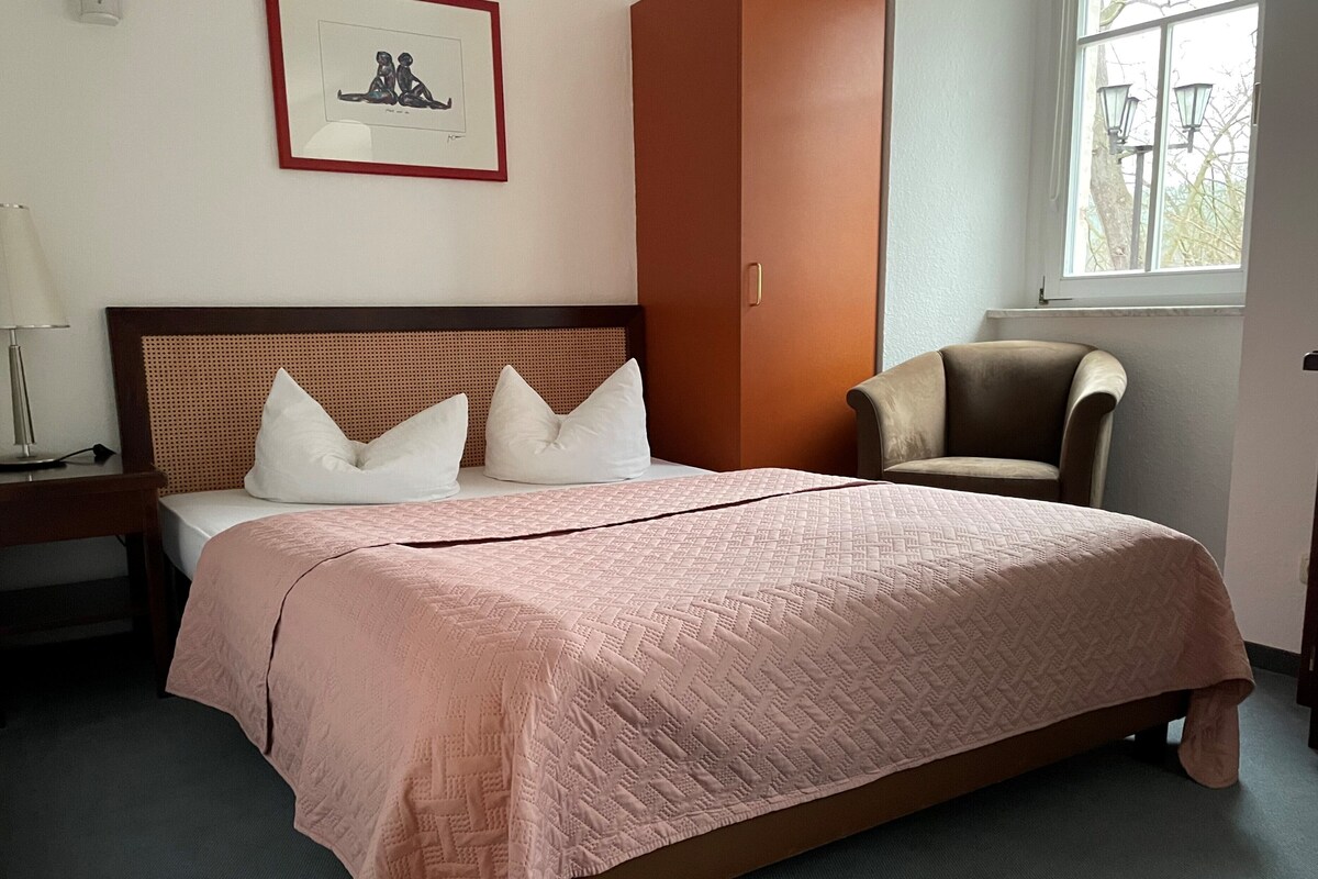 A neatly made bed with a pink quilt, a wooden headboard, and a framed picture on the wall.