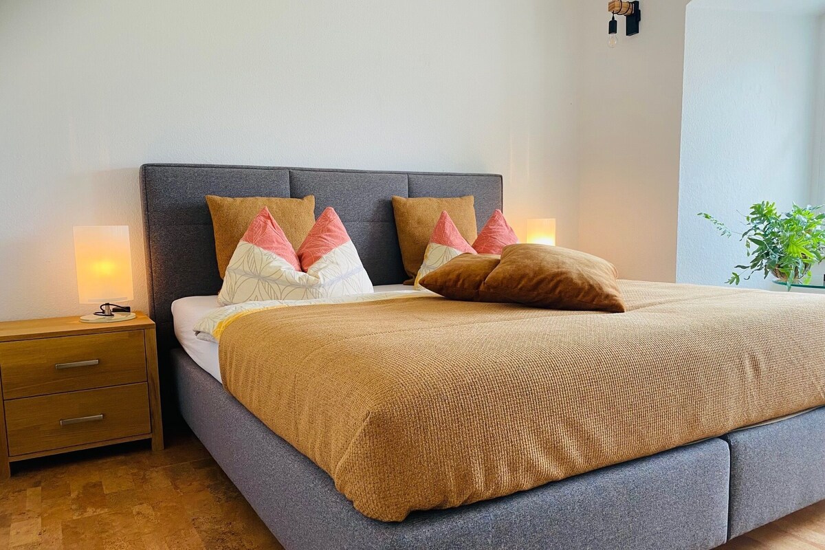 A neatly made bed with a grey headboard, multiple pillows, and a brown blanket.