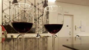 Dos copas de vino sobre una superficie reflectante, con una compleja estructura metálica al fondo.
