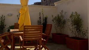 Un patio con muebles de madera y un paraguas amarillo, con vista a un edificio histórico de piedra con un campanario.