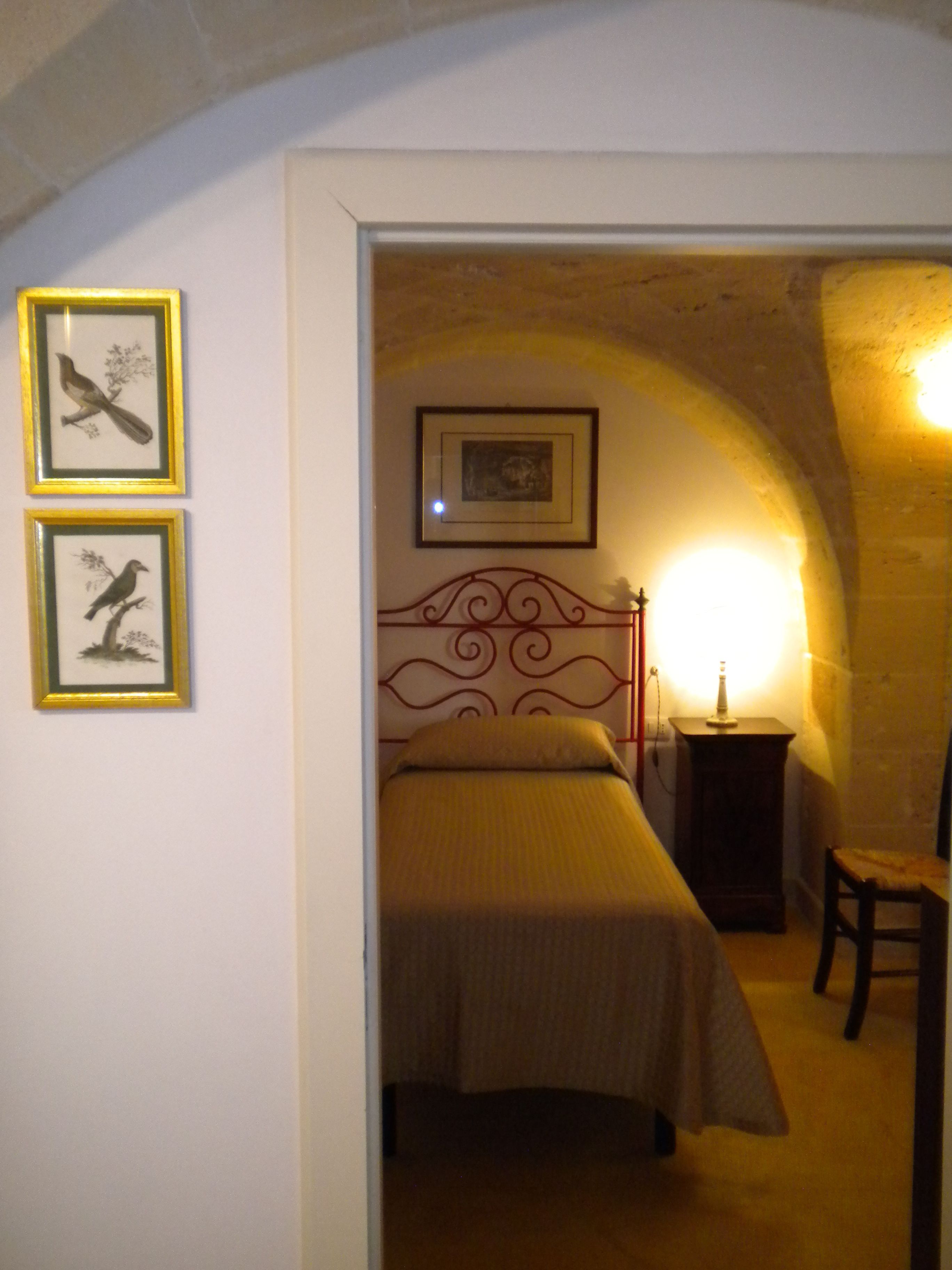 A bedroom with a bed, a chair, a nightstand, and framed pictures on the wall.