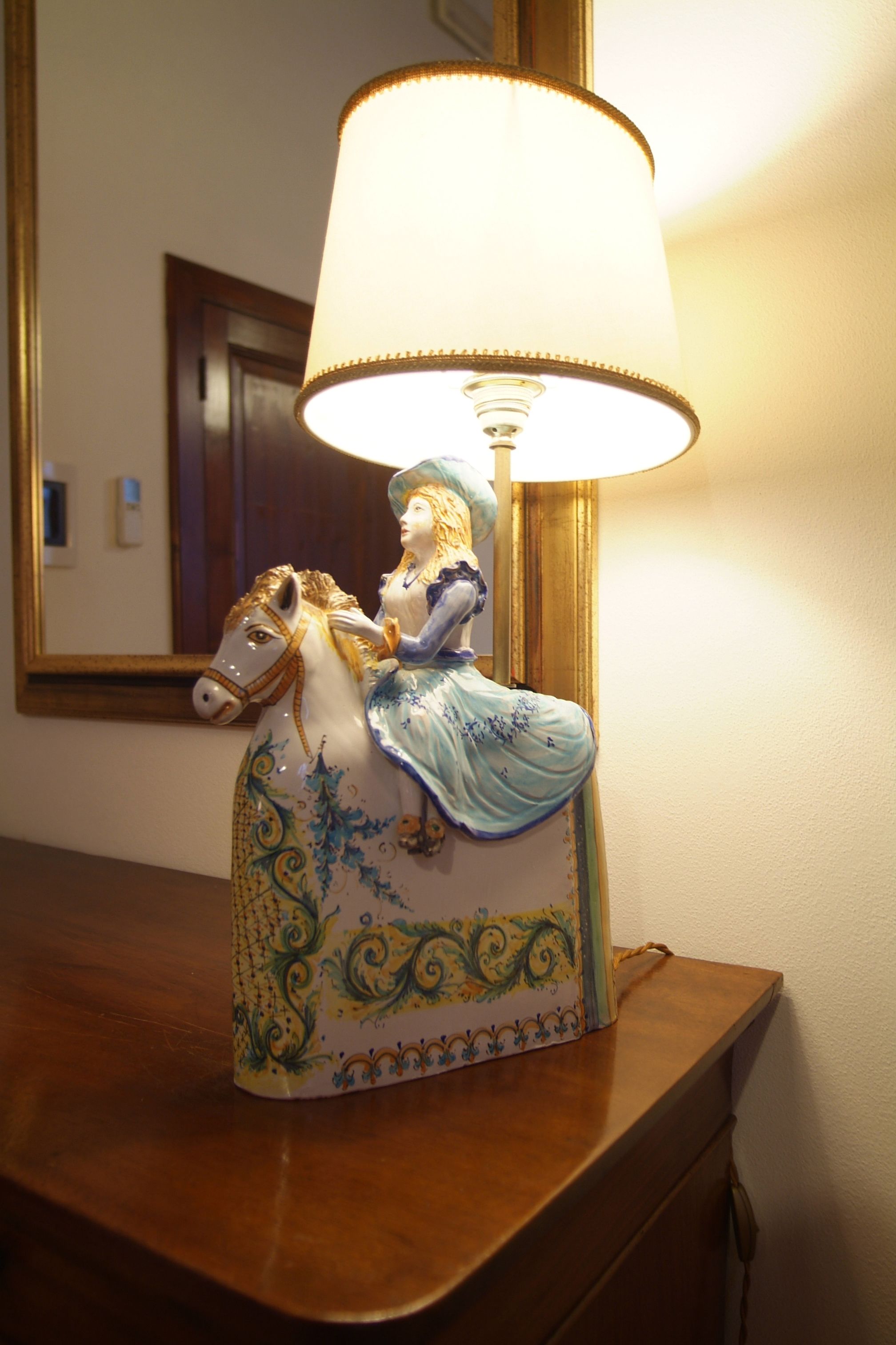 Una lampada decorativa con una statuetta di una donna a cavallo, posata su una superficie in legno.