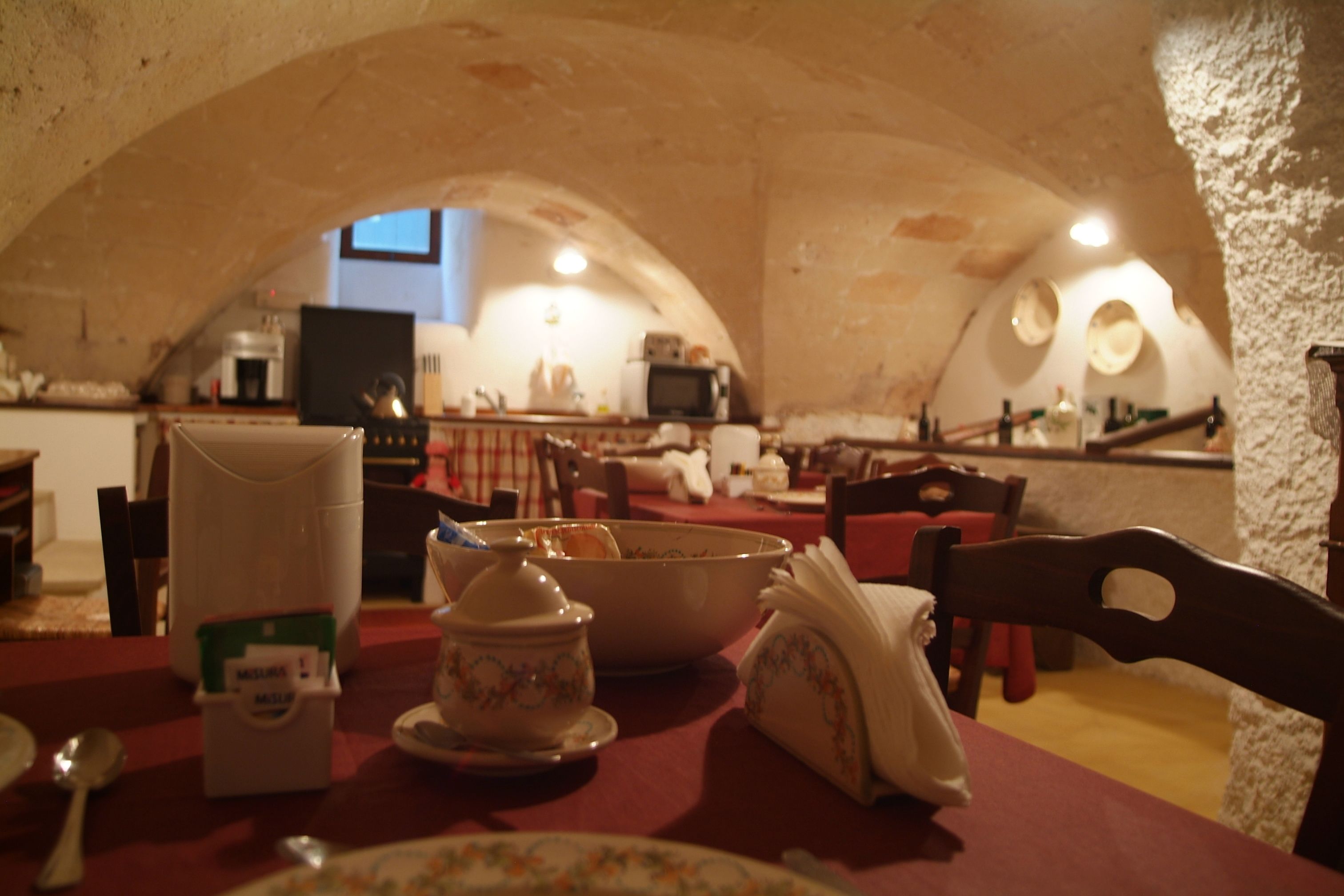 A dining area with a table set for two, a kitchen in the background, and a vaulted ceiling.