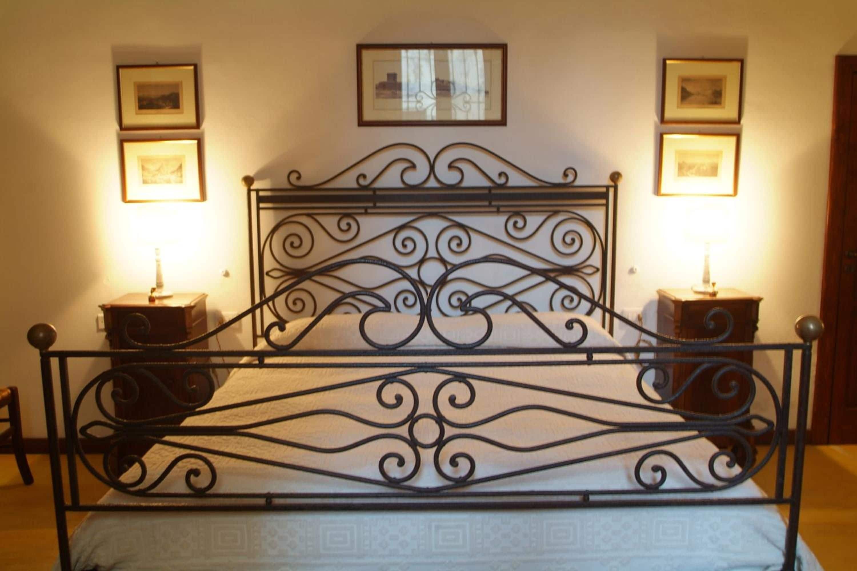 A bed with a wrought iron headboard, two bedside tables, and framed pictures on the walls.