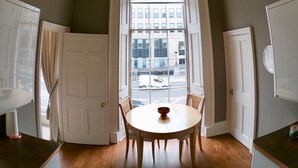 A dining area with a round table, chairs, a chandelier, and a view through a large window.