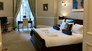 A hotel room with a large bed, a desk, a chair, a TV, and a window with curtains.