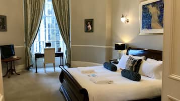 A hotel room with a large bed, a desk, a chair, a TV, and a window with curtains.