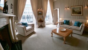 A spacious living room with a fireplace, two white sofas with blue cushions, a wooden coffee table, and large windows with curtains.