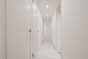 A narrow, well-lit hallway with white walls and a tiled floor, leading to a door with a no-smoking sign. - Hatch NAGAHORI 802 (Osaka)