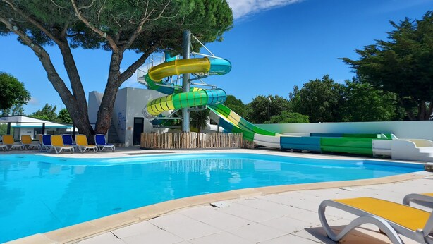 Una piscina con tobogán de agua, sillas de descanso y árboles.