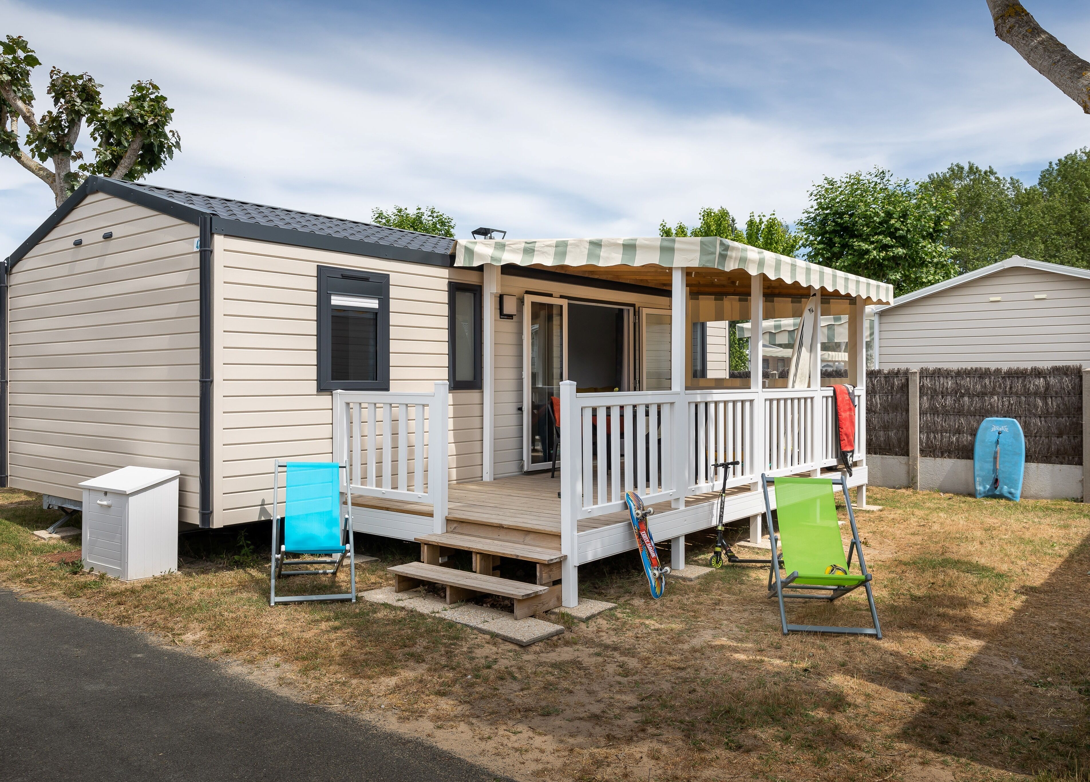A mobile home with a porch, a small deck, and a fenced backyard.