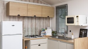 Una cocina compacta con armarios de madera, microondas integrado, estufa a gas y un lavamanos.